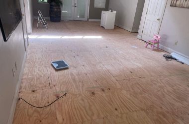 A living room with plywood flooring and a tv, in need of house leveling.