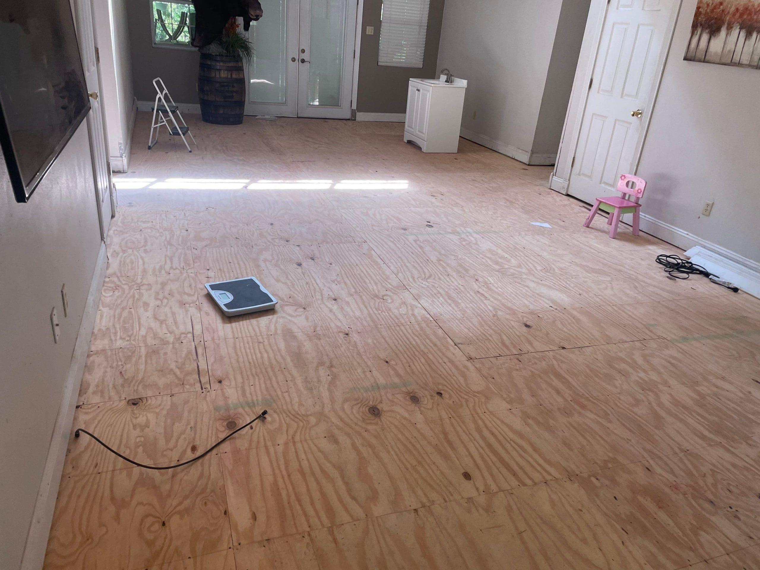 A living room with plywood flooring and a tv, in need of house leveling.