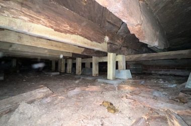 A basement with wooden beams and a wooden floor in need of foundation repair.
