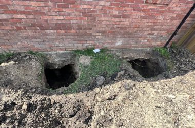 A foundation repair hole next to a brick house.