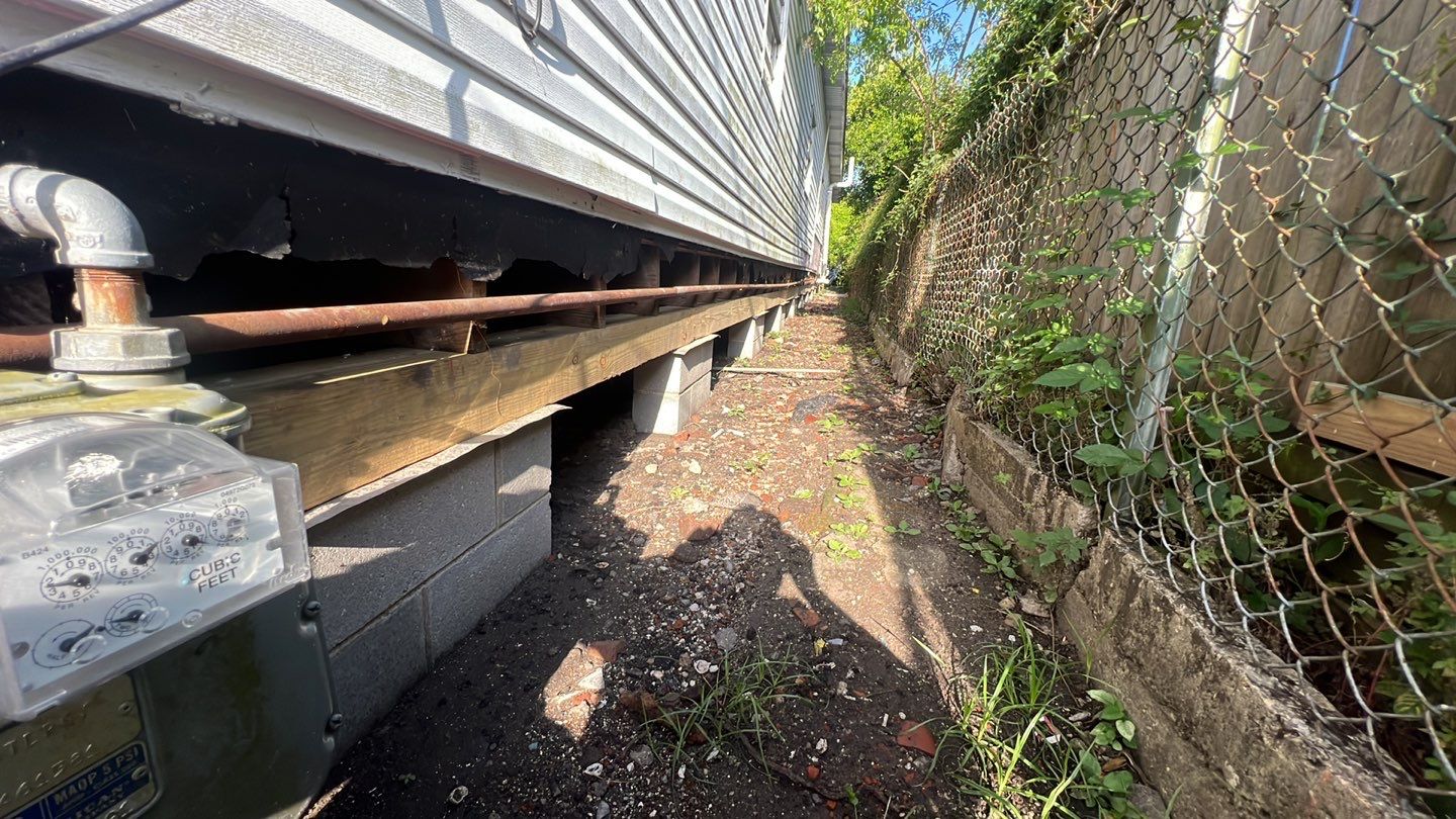 A house with a foundation repair needed and a fence next to it.