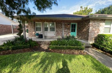 A small house with a green lawn and bushes needing foundation repair.