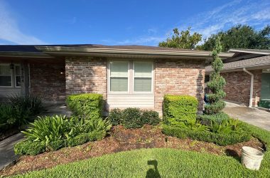 A brick home with bushes in front of it requiring foundation repair.