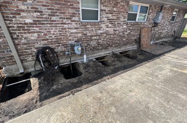 A house undergoing foundation repair with a hose and pipe in front of it.