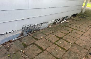A metal grate on the side of a house for foundation repair.