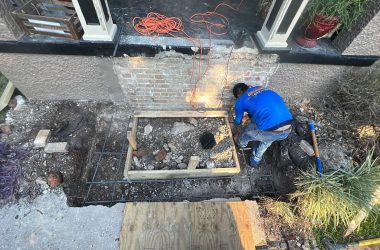 A man is working on a brick wall in front of a house, conducting foundation repair.