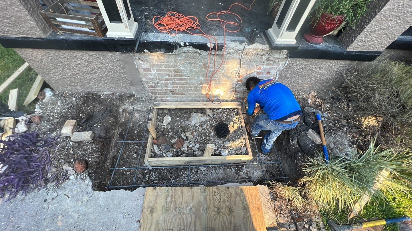A man is working on a brick wall in front of a house, conducting foundation repair.