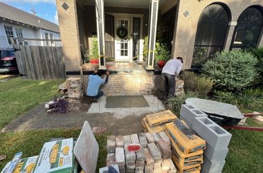 A man is laying bricks on the front steps of a house undergoing foundation repair.