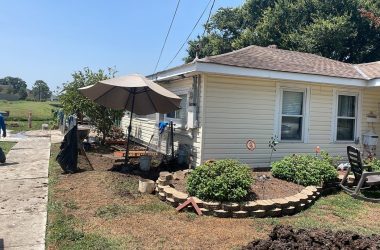 A small backyard with a lawn mower and an umbrella needing foundation repair.