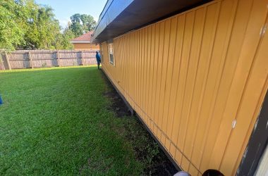 A backyard with yellow siding and a lawn mower.