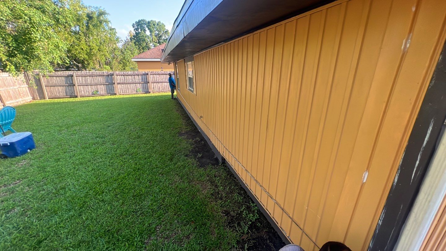 A backyard with yellow siding and a lawn mower.