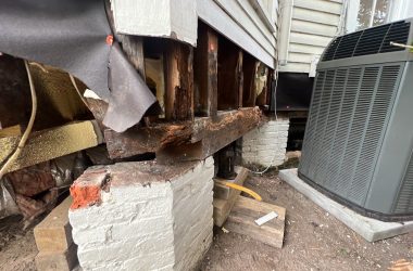 A damaged air conditioner in front of a house.