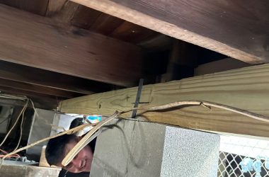 A man is working on a wooden beam under a house.