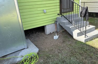 A green house with steps and a hose next to it.