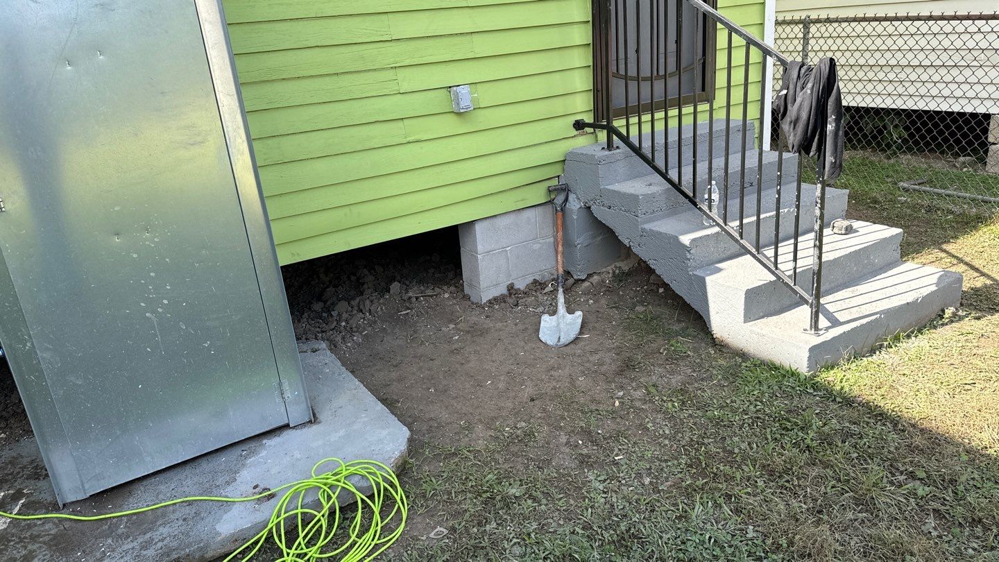 A green house with steps and a hose next to it.