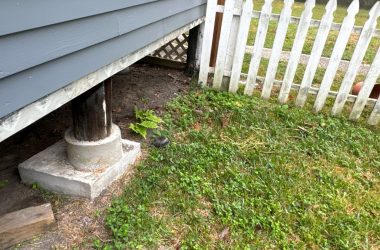 A white picket is next to a gray house.