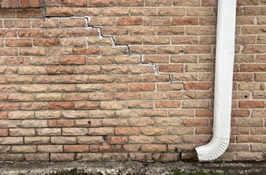 A damaged brick wall adjacent to a white pipe, indicating potential need for foundation repair.