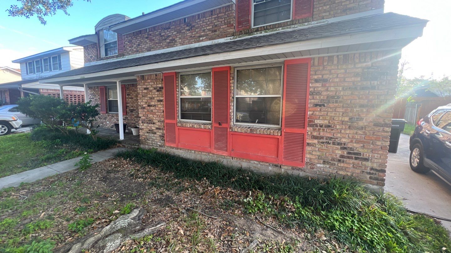 A brick house with red shutters and a car parked in front of it that requires foundation repair.