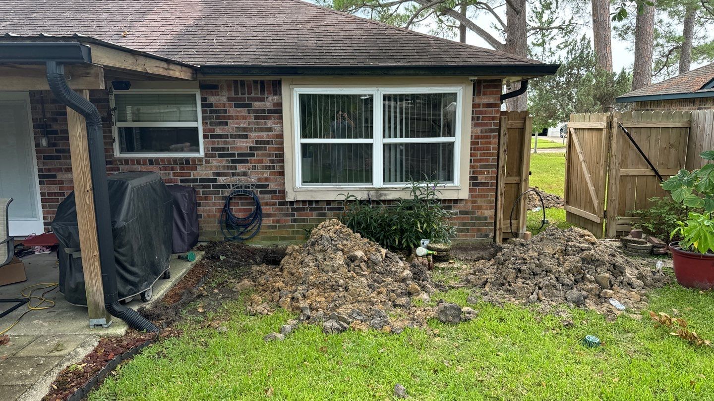 A backyard of a brick house in Slidell, Louisiana, with piles of dirt beside a window. A covered grill and an air conditioning unit are visible on the left side, and a wooden fence can be seen on the right, hinting at possible foundation issues.