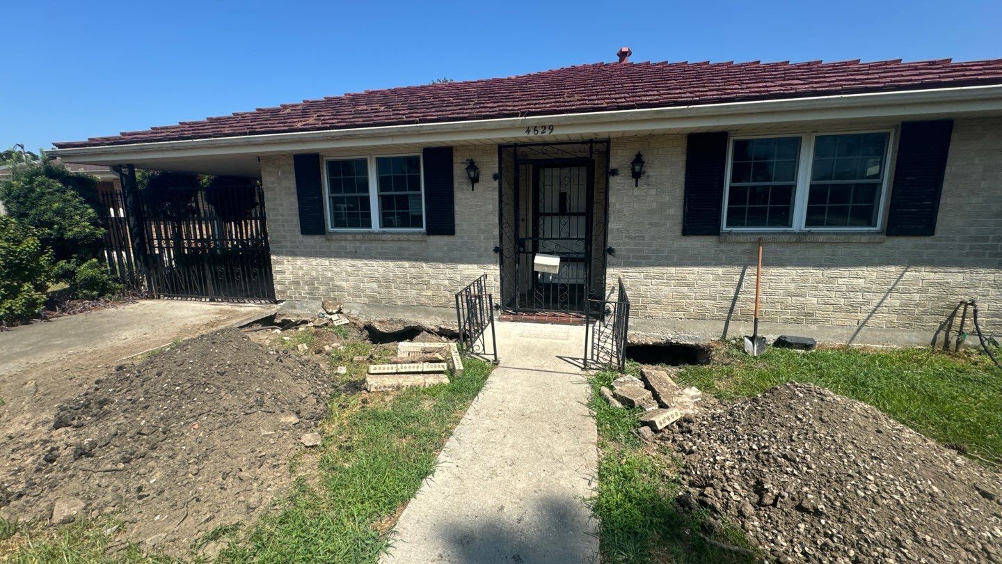 A single-story brick house with black shutters, a red roof, and a metal front door. There is a concrete walkway leading to the entrance, and piles of dirt on both sides of the path. Yearly foundation inspections are recommended for homes in Biloxi on the Mississippi Coast to maintain structural integrity.