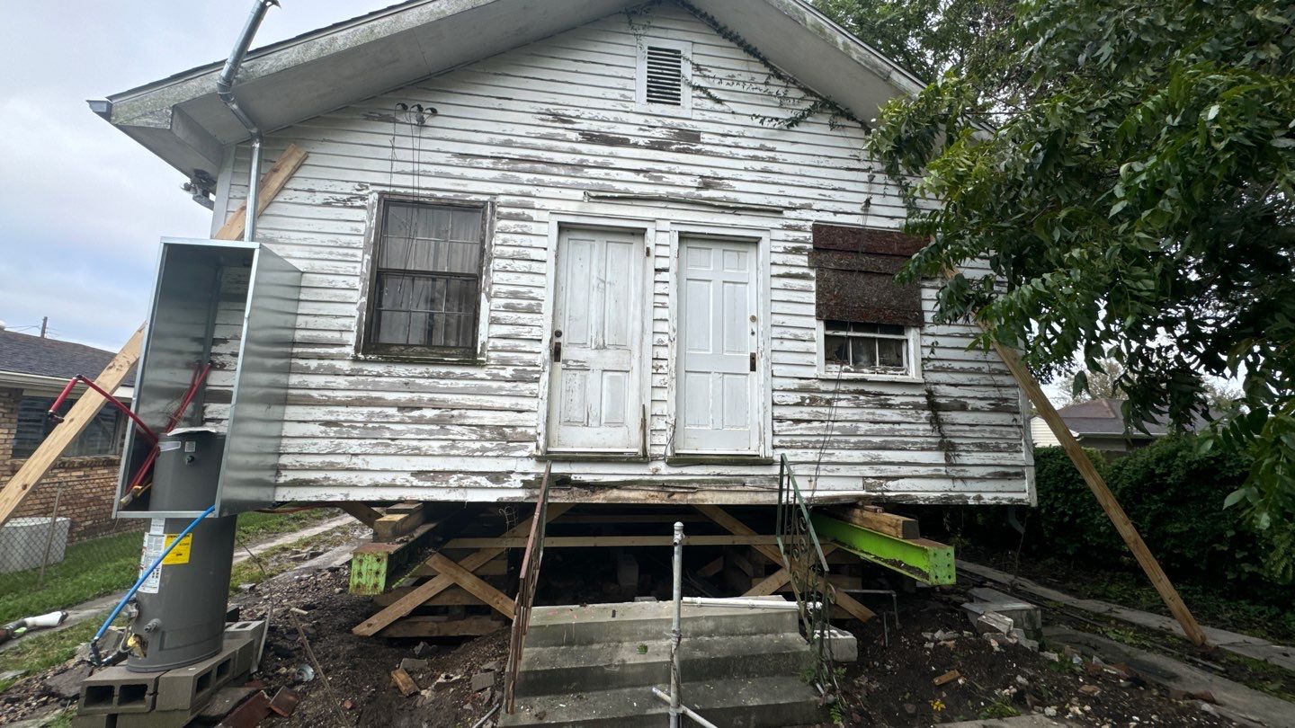 A weathered, elevated white house in Metairie is currently undergoing renovation, supported by wooden beams and a green metal frame courtesy of Jefferson Parish's expert house leveling services.