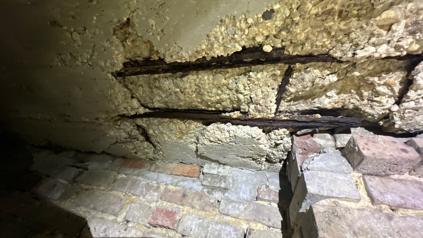 Exposed rusted rebar and cracked concrete in a dilapidated ceiling above a brick wall highlight the importance of proper foundation preparation for New Orleans residents.