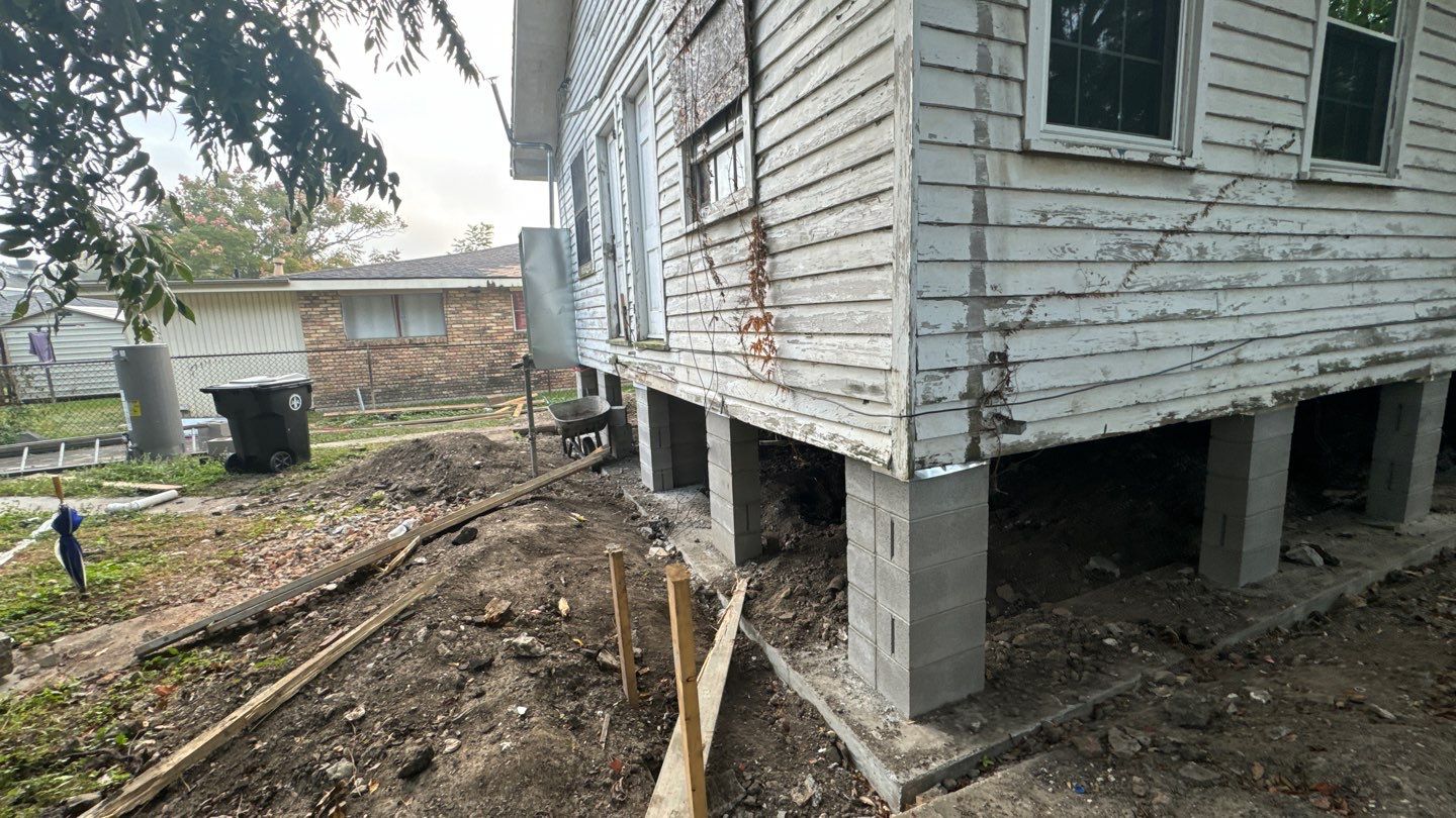 A house in New Orleans is elevated on concrete blocks during foundation repair, with tools and wood scattered around the dirt yard, highlighting a crucial step in home leveling.