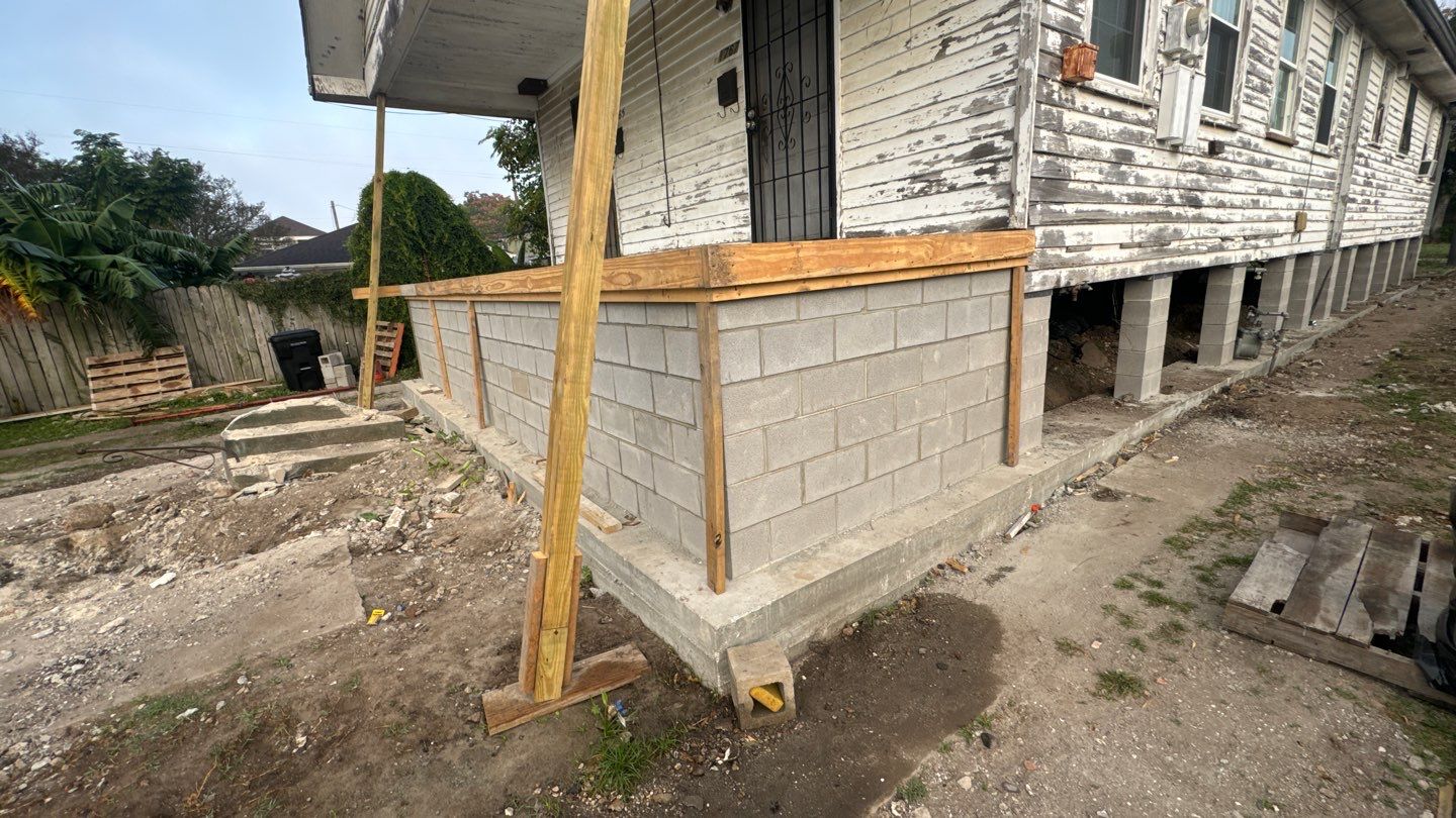 A partially constructed porch with a cinder block wall and wooden frame stands attached to a weathered New Orleans house. Dirt and debris are scattered around the site, hinting at ongoing renovations that might benefit from a Guide 2024 home leveling reference.