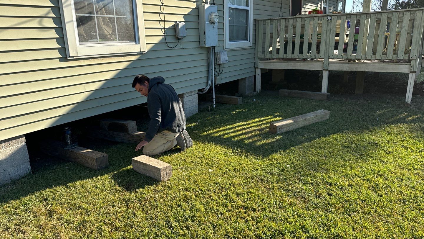 A person kneels on the grass beside a house in Louisiana, carefully inspecting the pier and beam foundation.