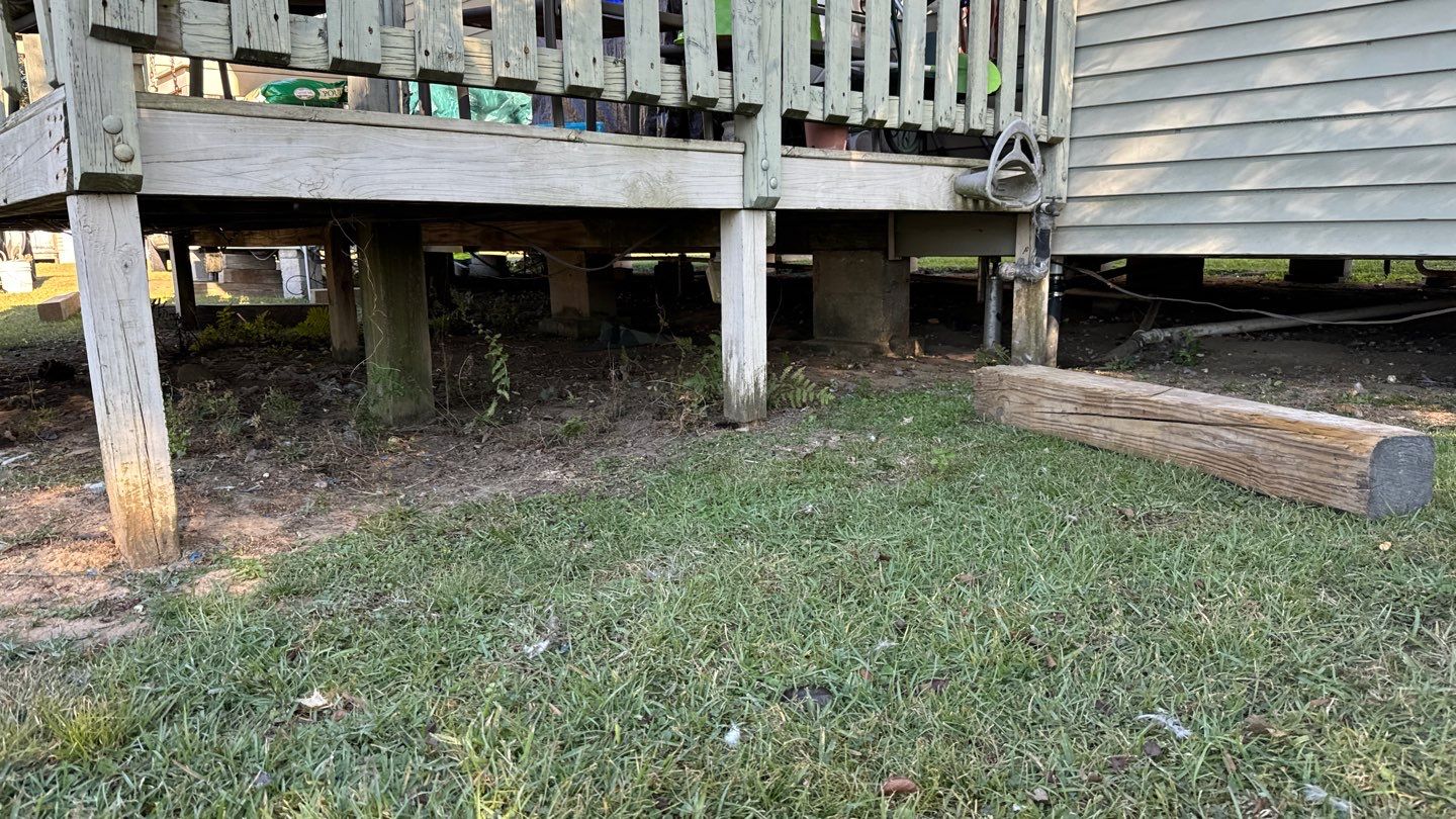A wooden deck with visible support beams and railing, reminiscent of those found in charming coastal homes, stands beautifully adjacent to a sturdy wooden beam on lush Louisiana grass.