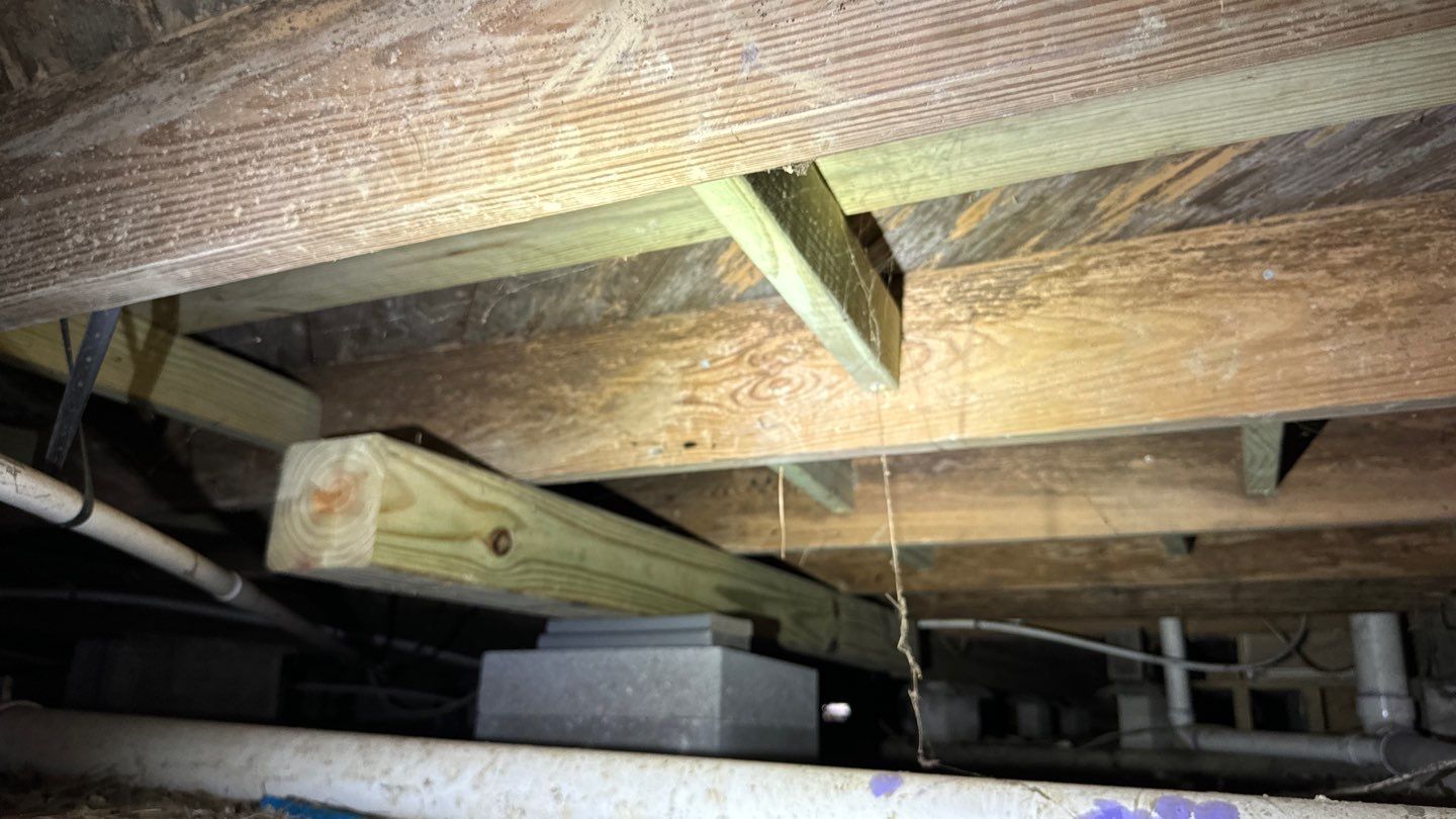 Wooden beams and pipes in a dimly lit crawl space, with visible insulation and electrical components, hinting at possible foundation issues common in the humid climate of St. Tammany Parish, Louisiana.