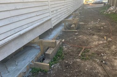 House undergoing foundation repair with wooden supports underneath. Dirt ground and construction materials visible, showcasing effective solutions for foundation problems faced by New Orleans homeowners.