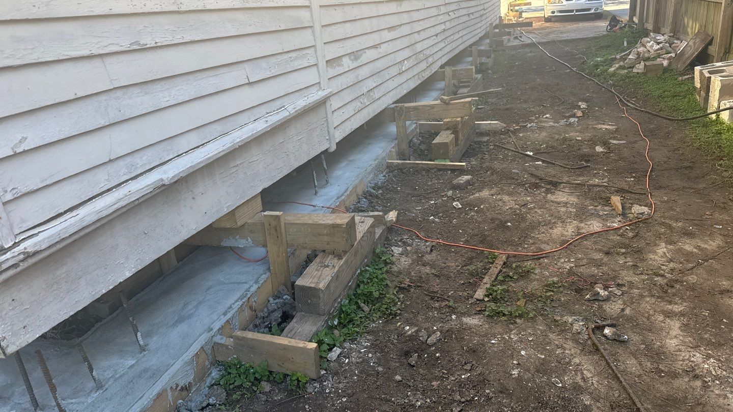 House undergoing foundation repair with wooden supports underneath. Dirt ground and construction materials visible, showcasing effective solutions for foundation problems faced by New Orleans homeowners.