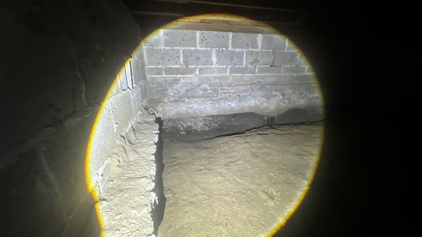 A flashlight illuminates a dimly lit basement in St. Tammany Parish, revealing rough concrete walls and an uneven dirt floor, hinting at potential foundation issues.