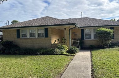 The single-story brick house with a sloped roof, front porch, and black shutters rests on a solid home's foundation. Its well-maintained yard features a concrete walkway and vibrant plants, providing ideas on what to do for enhancing curb appeal.